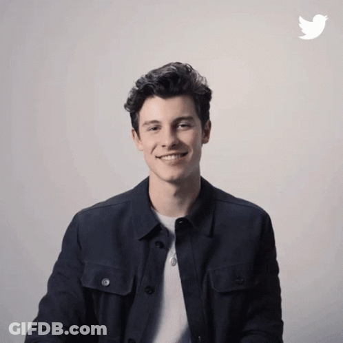 A Man In A Black Jacket Is Smiling In Front Of A Twitter Icon GIF