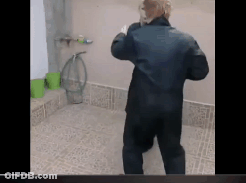 A Man In A Black Jacket Is Standing In A Bathroom Talking On A Phone . GIF