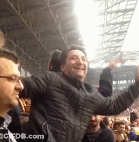 A Man In A Black Jacket Is Standing In A Crowd Of People . GIF