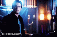 A Man In A Black Jacket Is Standing In A Dark Room Looking At The Camera GIF