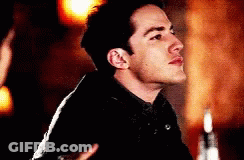 A Man In A Black Jacket Is Standing In A Dark Room . GIF