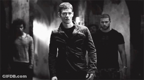 A Man In A Black Jacket Is Standing In A Dark Room GIF
