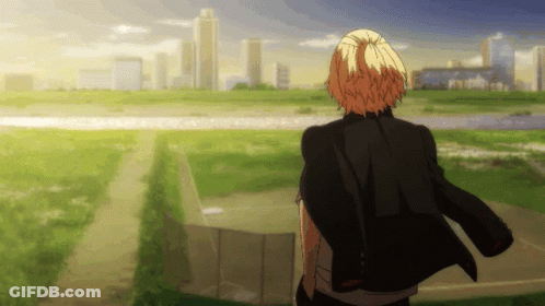 A Man In A Black Jacket Is Standing In A Field Looking At A City Skyline GIF