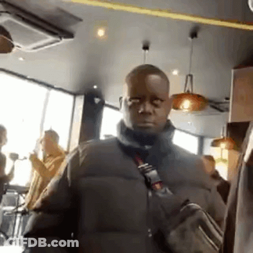 A Man In A Black Jacket Is Standing In A Restaurant With A Bag On His Shoulder . GIF