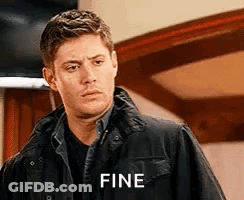 A Man In A Black Jacket Is Standing In A Room With The Word Fine Written On His Chest . GIF