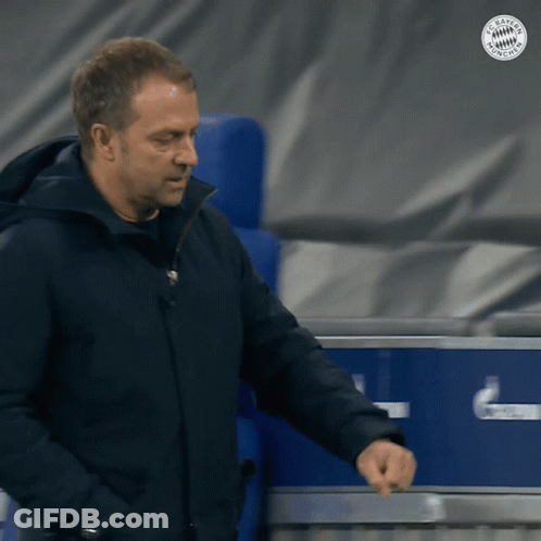 A Man In A Black Jacket Is Standing In Front Of A Blue Box That Says Fc Bayern Munich GIF