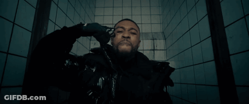 A Man In A Black Jacket Is Standing In Front Of A Blue Tiled Wall GIF