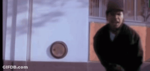A Man In A Black Jacket Is Standing In Front Of A Clock On A Wall . GIF