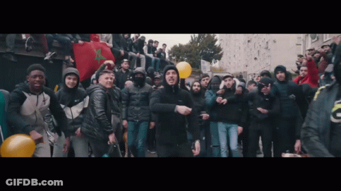 A Man In A Black Jacket Is Standing In Front Of A Crowd Of People GIF