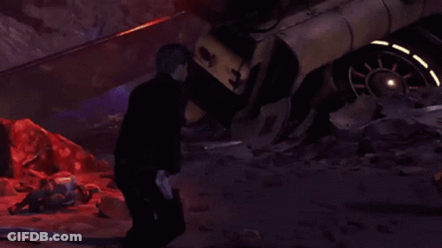 A Man In A Black Jacket Is Standing In Front Of A Destroyed Car GIF