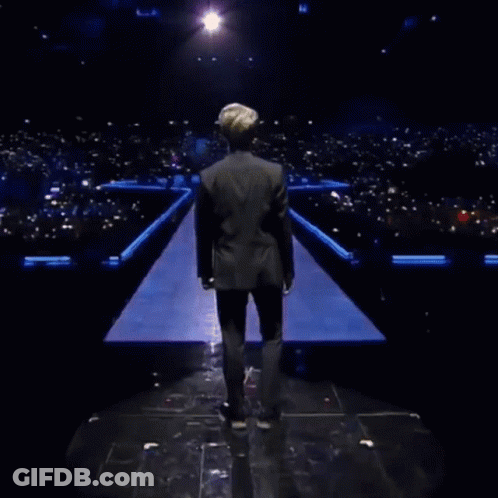 A Man In A Black Jacket Is Standing In Front Of A Field Of Skulls GIF