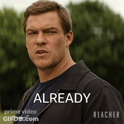 A Man In A Black Jacket Is Standing In Front Of A Sign That Says " Already " GIF