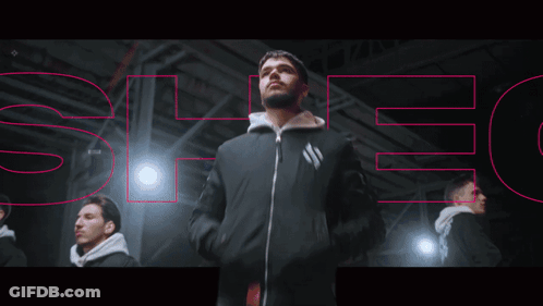 A Man In A Black Jacket Is Standing In Front Of A Sign That Says " Spec " GIF