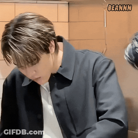 A Man In A Black Jacket Is Standing In Front Of A Wall With Beannn Written On It GIF