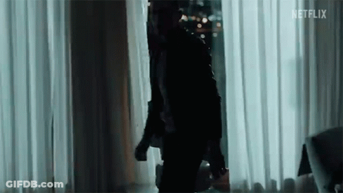 A Man In A Black Jacket Is Standing In Front Of A Window In A Room . GIF