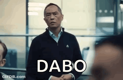 A Man In A Black Jacket Is Standing In Front Of A Window With The Word Dabo Written On His Face . GIF