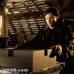 A Man In A Black Jacket Is Standing Next To A Large Box GIF
