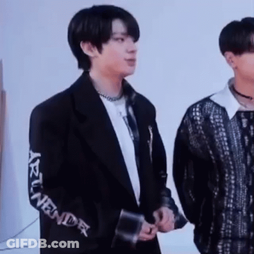 A Man In A Black Jacket Is Standing Next To Another Man In A Black Shirt . GIF