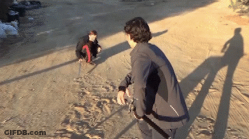 A Man In A Black Jacket Is Standing On A Dirt Road Next To Another Man GIF