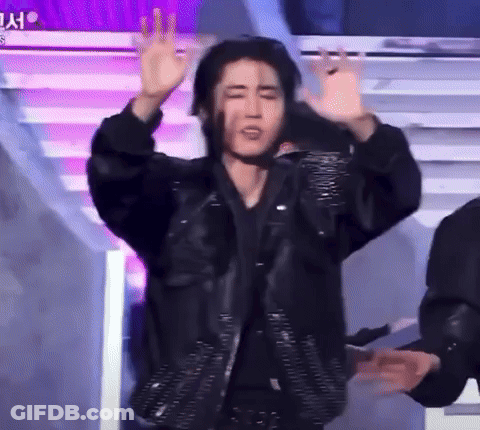 A Man In A Black Jacket Is Standing On A Stage With His Arms Outstretched . GIF