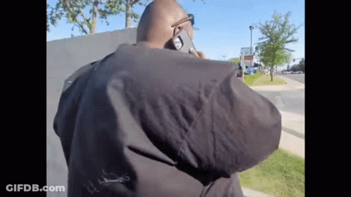 A Man In A Black Jacket Is Talking On A Cellphone GIF