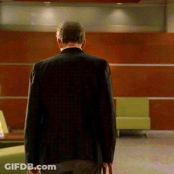 A Man In A Black Jacket Is Walking In A Room GIF