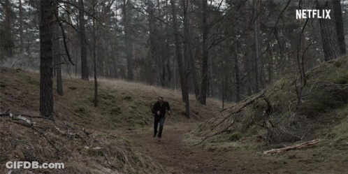 A Man In A Black Jacket Is Walking Through A Dark Forest With A Netflix Logo In The Background GIF