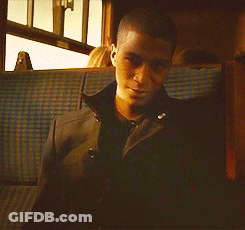 A Man In A Black Jacket Sits In A Blue Plaid Seat On A Train GIF