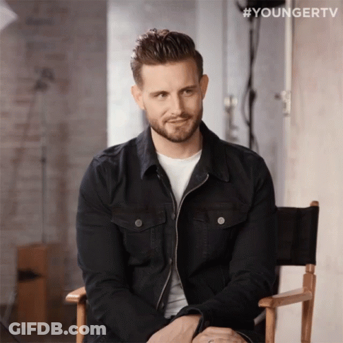 A Man In A Black Jacket Sits In A Director 'S Chair With #Youngertv Written Above Him GIF