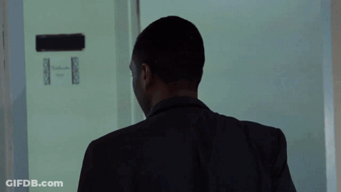 A Man In A Black Jacket Stands In A Room GIF