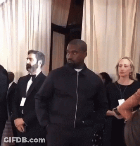 A Man In A Black Jacket Stands In A Room With Other People GIF