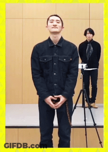 A Man In A Black Jacket Stands In Front Of A Camera GIF