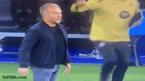 A Man In A Black Jacket Stands Next To A Man In A Yellow Nike Shirt GIF