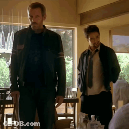 A Man In A Black Jacket Stands Next To Another Man GIF