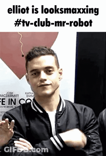 A Man In A Black Jacket With His Arms Crossed Is Standing In Front Of A Red Heart . GIF