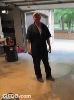 A Man In A Black Jumpsuit Is Standing In Front Of A Garage Door . GIF
