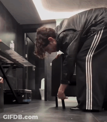 A Man In A Black Leather Jacket And White Stripped Pants Is Bending Over GIF