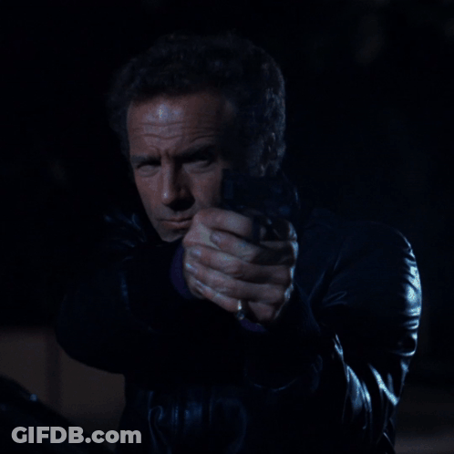 A Man In A Black Leather Jacket Is Holding A Gun In His Hand GIF