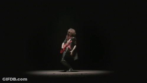 A Man In A Black Leather Jacket Is Playing A Red Electric Guitar In The Dark . GIF