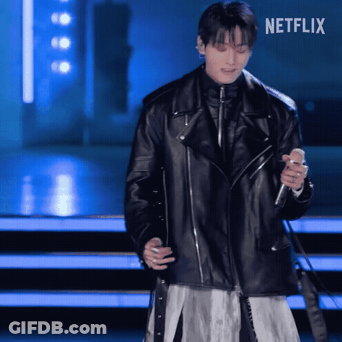 A Man In A Black Leather Jacket Is Singing Into A Microphone With Netflix Written On The Bottom GIF