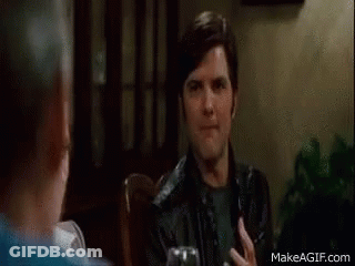 A Man In A Black Leather Jacket Is Sitting At A Table With A Glass Of Wine . GIF