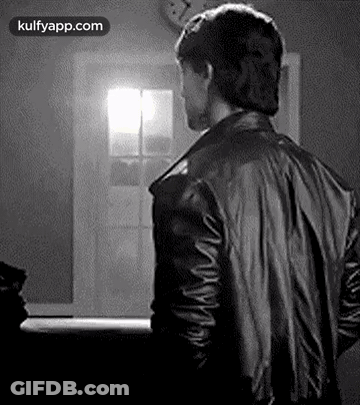 A Man In A Black Leather Jacket Is Standing In Front Of A Window . GIF
