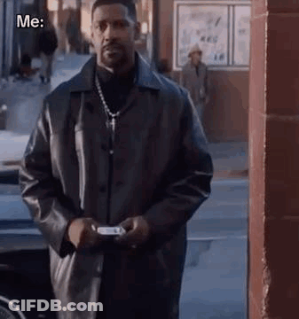 A Man In A Black Leather Jacket Is Standing On A Sidewalk Holding A Cell Phone . GIF