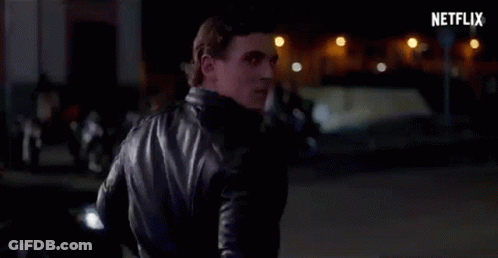 A Man In A Black Leather Jacket Is Standing On A Street At Night . GIF