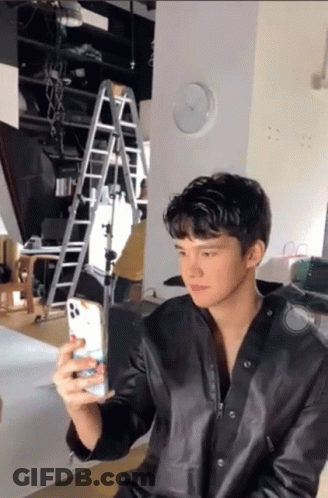 A Man In A Black Leather Jacket Is Taking A Picture Of Himself With His Phone GIF