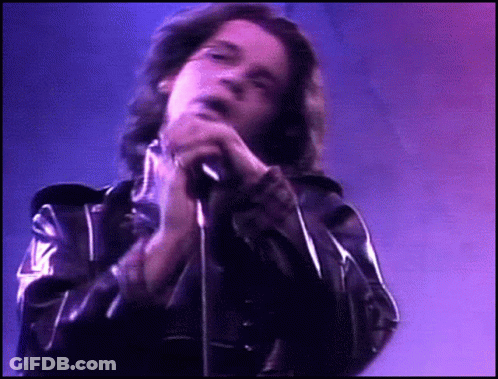 A Man In A Black Leather Jacket Singing Into A Microphone GIF