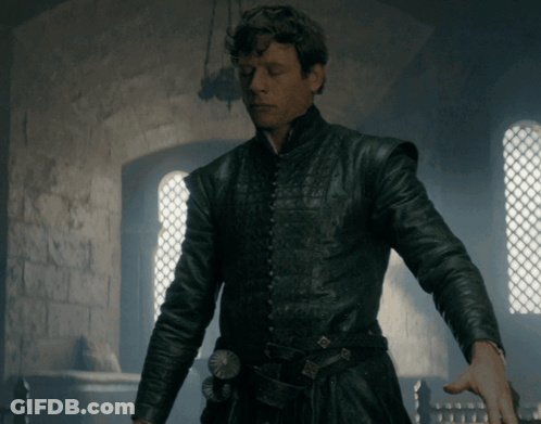 A Man In A Black Leather Jacket Stands In Front Of A Brick Wall GIF