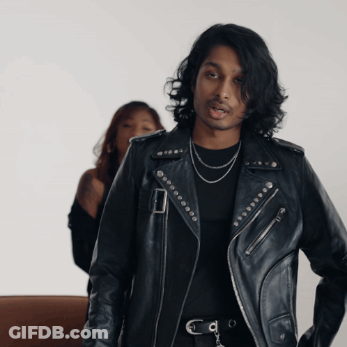 A Man In A Black Leather Jacket Stands Next To A Woman GIF