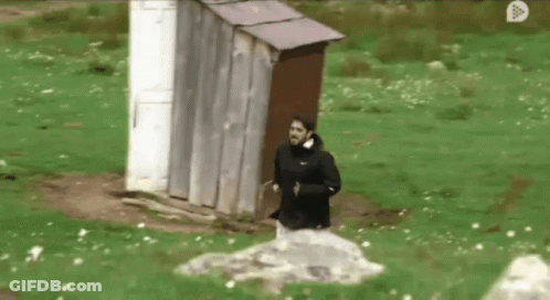 A Man In A Black Nike Jacket Is Running In Front Of An Outhouse GIF