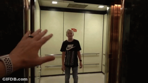 A Man In A Black Nike Shirt Is Standing In An Elevator GIF